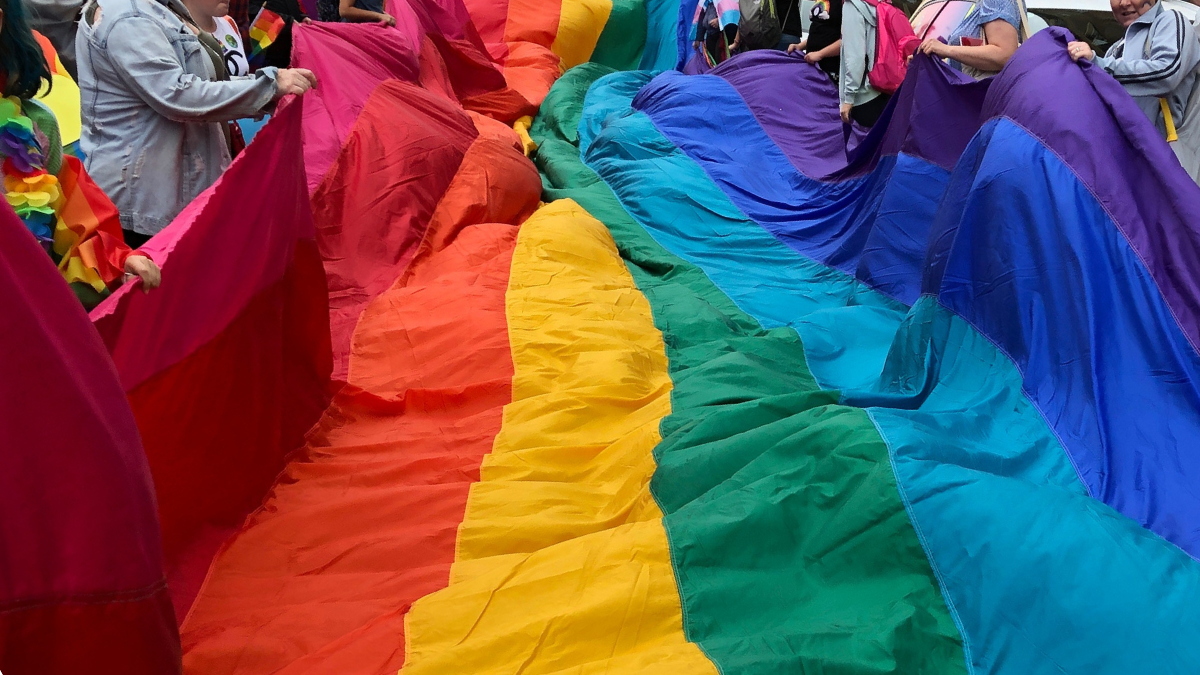 A giant rainbow flag being held by young people at Norwich Pride