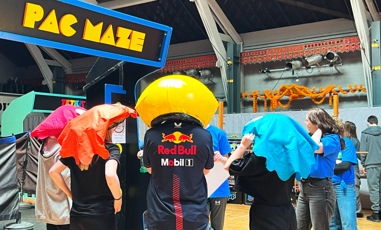 Six young people dress as ghosts from pac man (with coloured headgear to represent Blinky, Inky, Pinky and Clyde), with another young person donning a large Pac Man helmet, representing the game's eponymous hero.