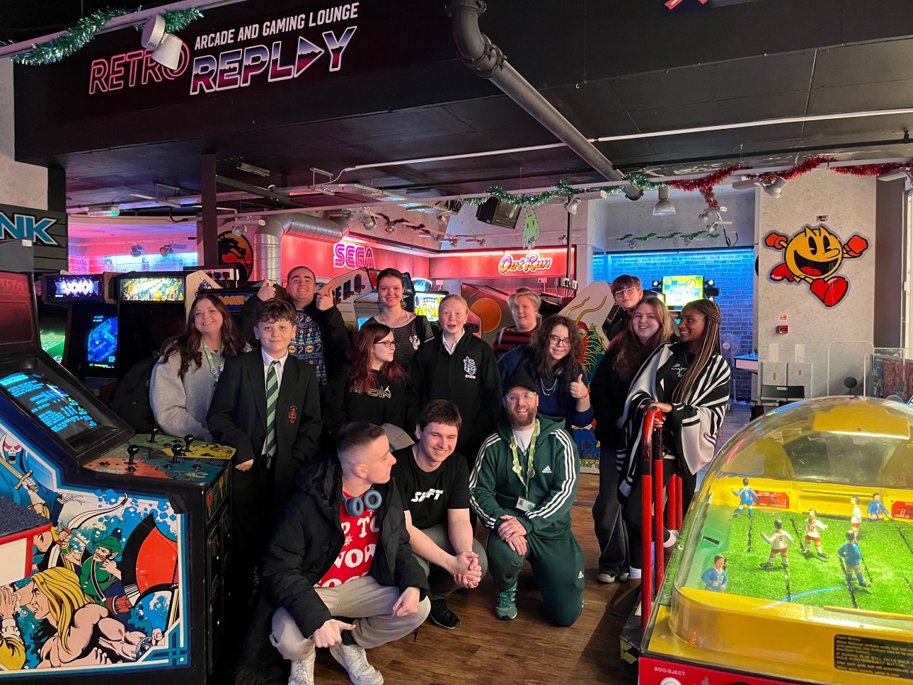 A group of young people representing the Norwich YAB pose for a photo in the Retro Replay Arcade in Norwich, surrounded by pinball machines and classic arcade cabinets.