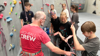 Instructor showing young person harness for climbing wall