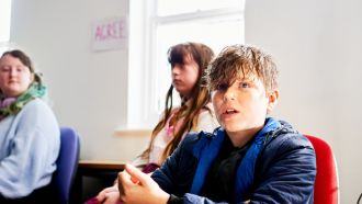 A young person speaking, with two other young people listening in the background