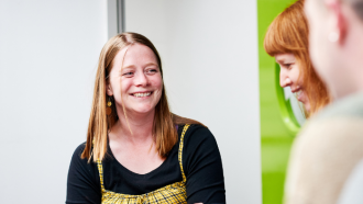 A staff member stood with their arms folded, smiling, chattging to other staff members