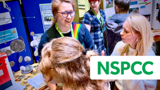 Youth worker stood at a YouthBank stall with NSPCC logo in the foreground
