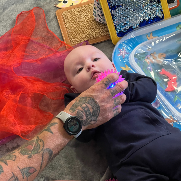 A baby looking at a small toy being held in front of their face