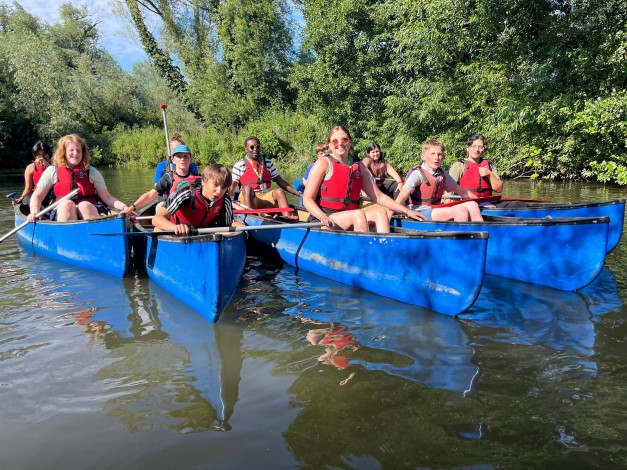 A group of young people in blue canoes travel down the river Yare