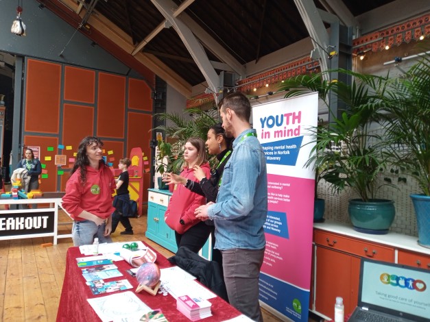 Youth workers stood behind a Youth in Mind stall talking to a young person