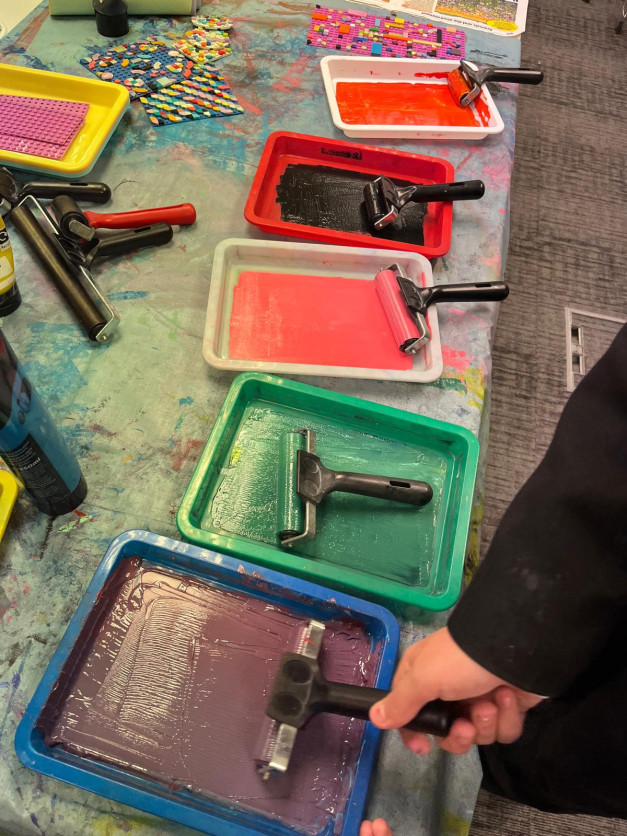 Some paint trays with rollers, containing different colours