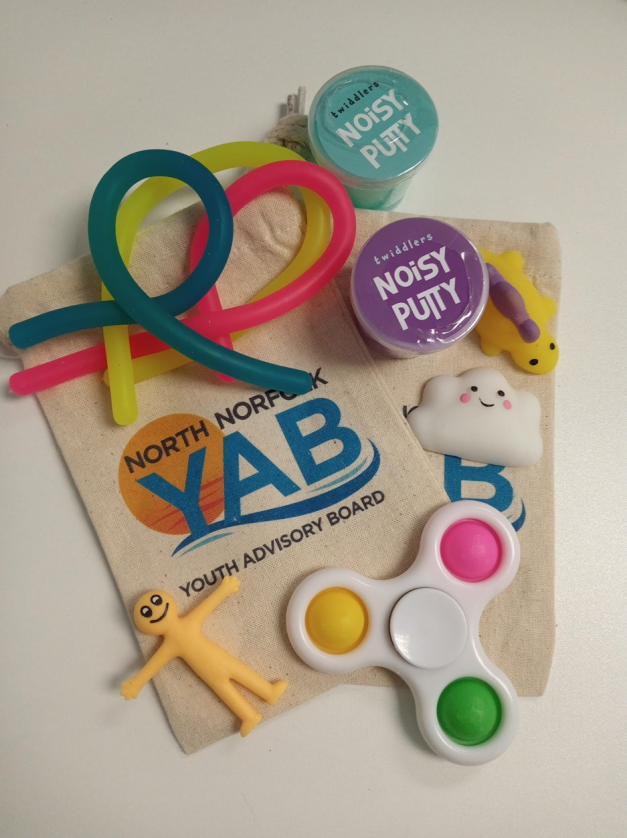 A colourful selection of sensory fidget toys arranged on a table, alongside a nice cotton bag