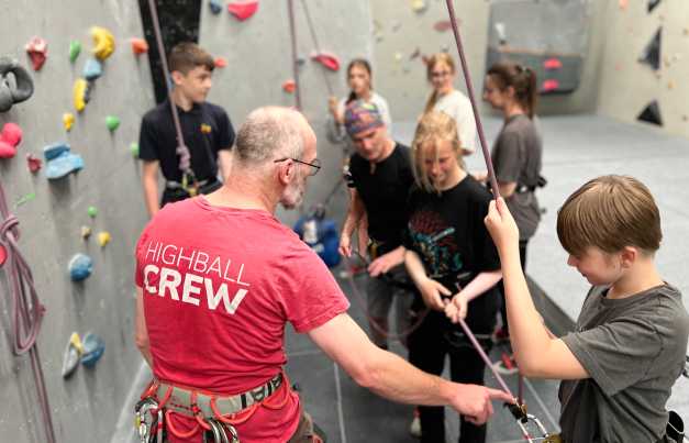 Instructor showing young person harness for climbing wall