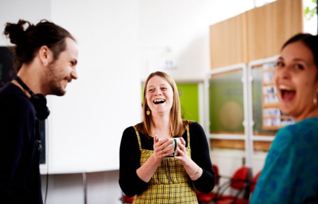 Three staff members smiling and laughing. The staff member in the middle is holding a mug