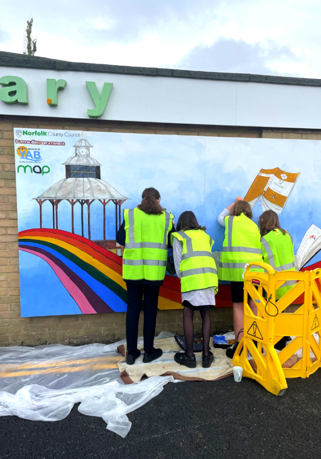 Young people painting a rainbow mural on the side of a library