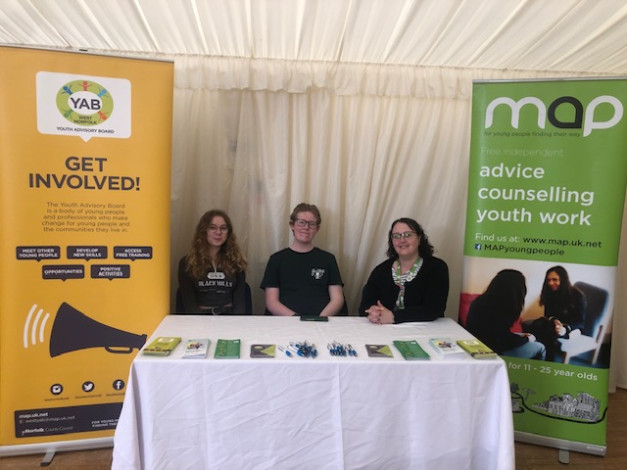 Young people sitting a desk with a yellow banner for the YAB behind them